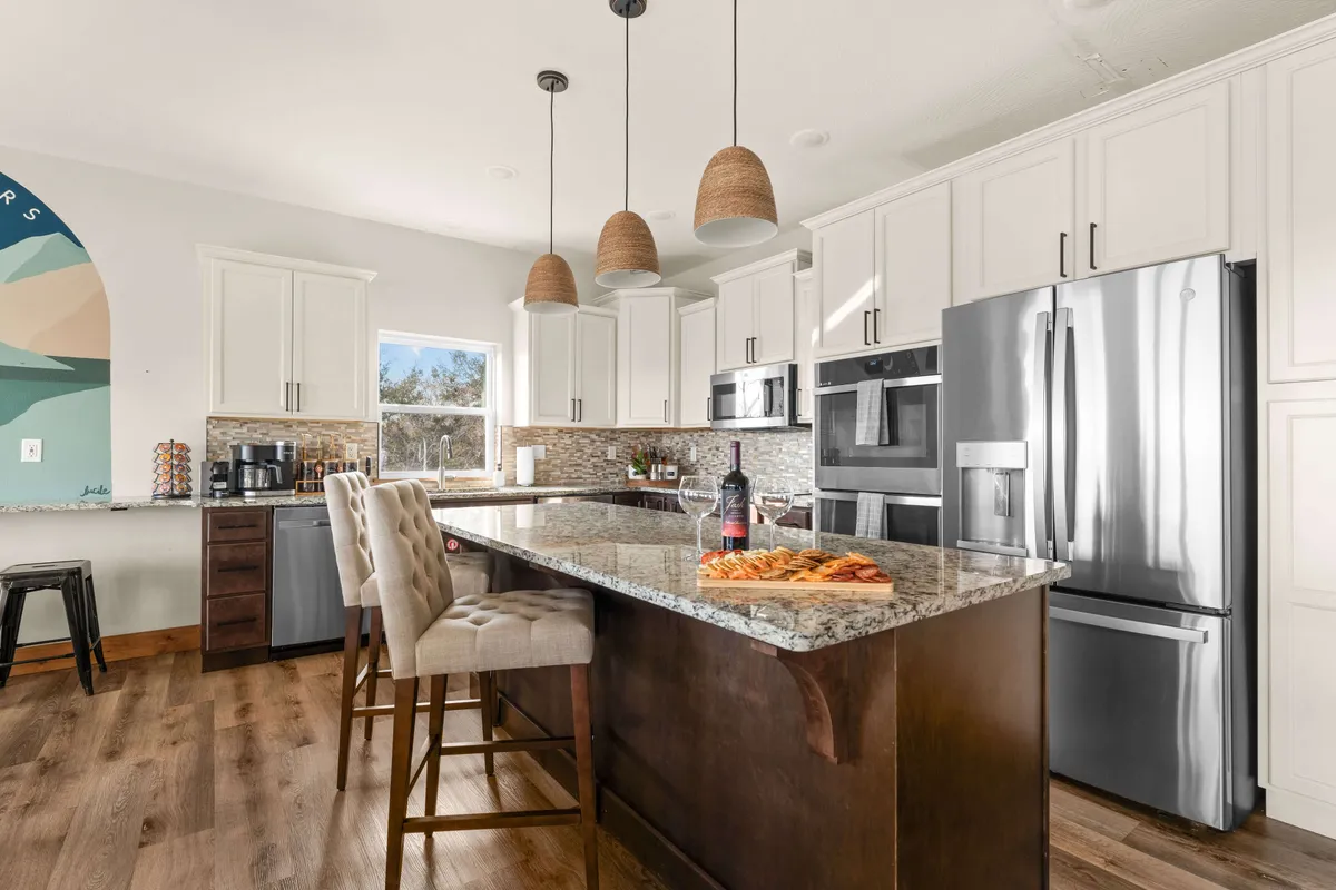 A contemporary kitchen featuring granite countertops, modern appliances, colorful wall mural, and hanging pendant lights. The space exudes a festive, welcoming atmosphere perfect for meal prep, casual dining, or festive feasts.