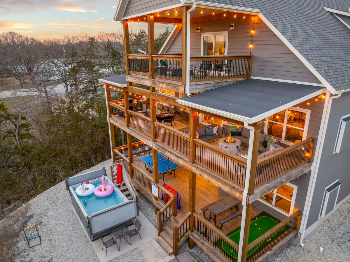 An expansive exterior entertaining area featuring multi-level decks, a hot tub (which can represent the private swim spa), string lights for ambiance, an outdoor pool table, and a putting green. The space exudes a cheerful, festive mood with several activity and relaxation zones visible, encouraging socializing and play.