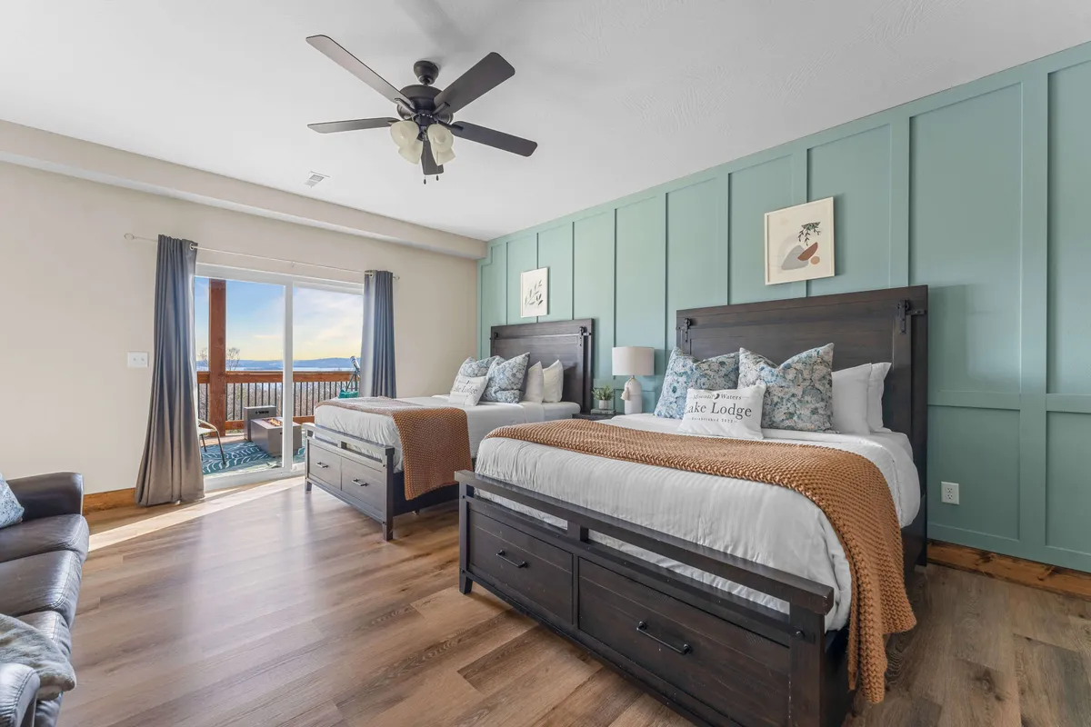 A cozy bedroom scene with two neatly made beds, decorative pillows, a ceiling fan, and a sliding glass door letting in plenty of natural light. The room is inviting and appears restful, with easy access to outdoor views, perhaps via a patio or balcony.