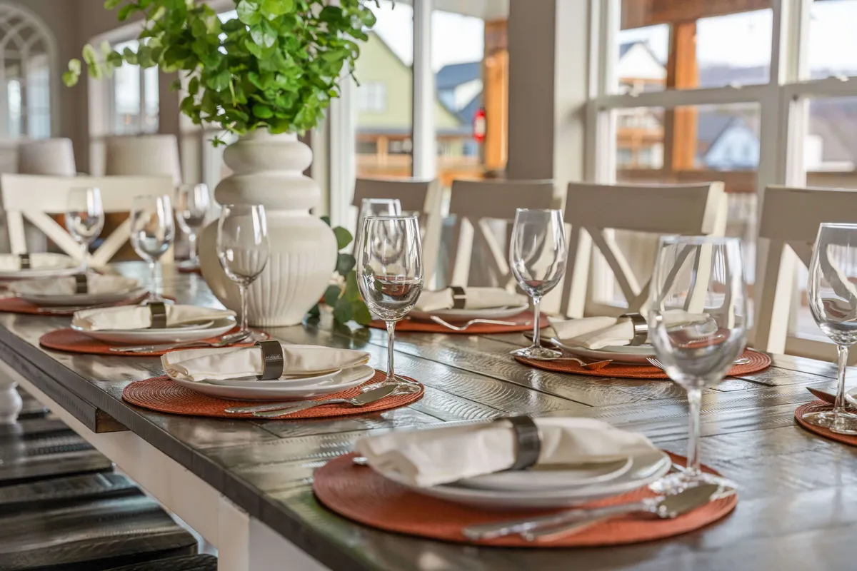A large dining table elegantly set with tableware and a lush greenery centerpiece. The arrangement sets a warm, welcoming stage for intimate dinners, festive group meals, or family gatherings adjacent to the kitchens.