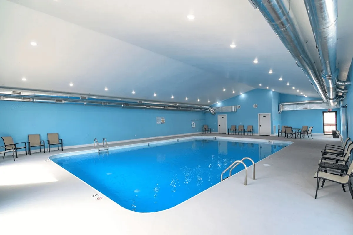 An inviting indoor swimming pool area with lounge chairs arranged along the poolside, surrounded by large windows that let in plentiful natural light. The space feels spacious and offers a tranquil spot for swimming, relaxing, and socializing.