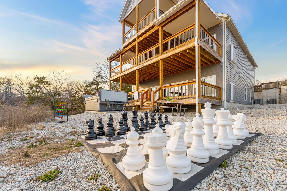 An exterior shot featuring a large outdoor chess set on a patio next to a multi-level deck, with scenic landscape surrounding the area. The playful setup and relaxed vibe encourage outdoor engagement and group activities.