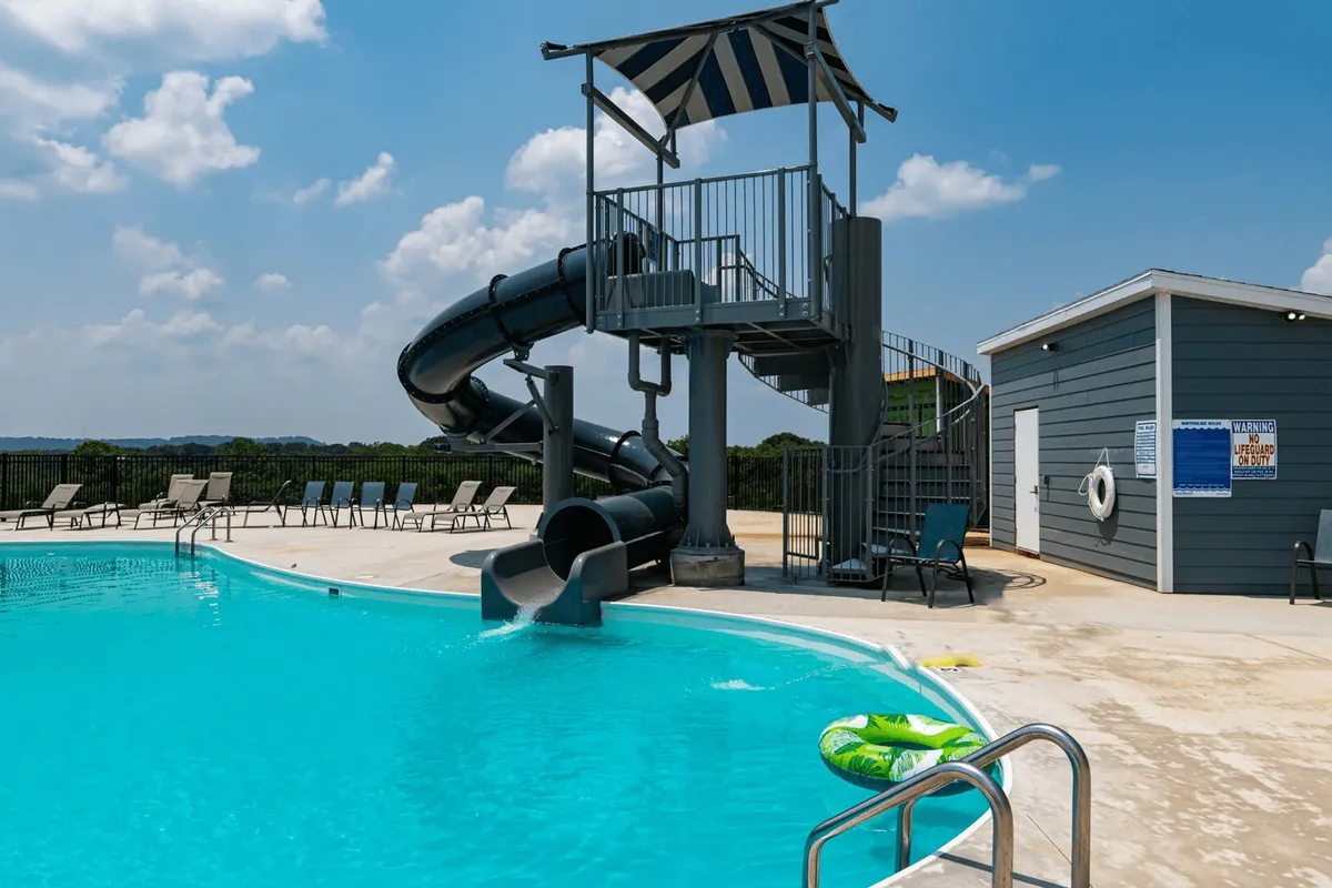 A sparkling outdoor swimming pool complete with a water slide and surrounding poolside chairs, radiating a joyful, resort-like atmosphere. Guests are visible enjoying the water and relaxing by the pool, reinforcing the excitement and recreational spirit.